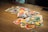 A scattered pile of brightly colored cards with various cartoon characters and numbers is spread out on a wooden table. In the center, an Uno card with distinctive red, blue, yellow, and green design is noticeable.