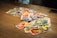 A scattered pile of brightly colored cards with various cartoon characters and numbers is spread out on a wooden table. In the center, an Uno card with distinctive red, blue, yellow, and green design is noticeable.