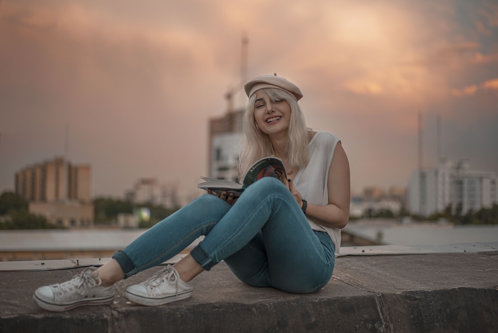 a woman sitting on a ledge reading a book