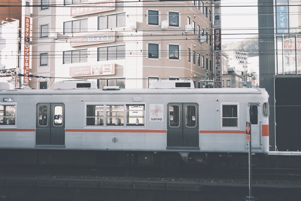 a silver train traveling down train tracks next to tall buildings