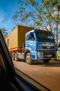 a blue truck driving down a road next to a forest
