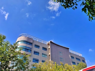 A modern building with clean lines surrounded by lush greenery under a bright sky.