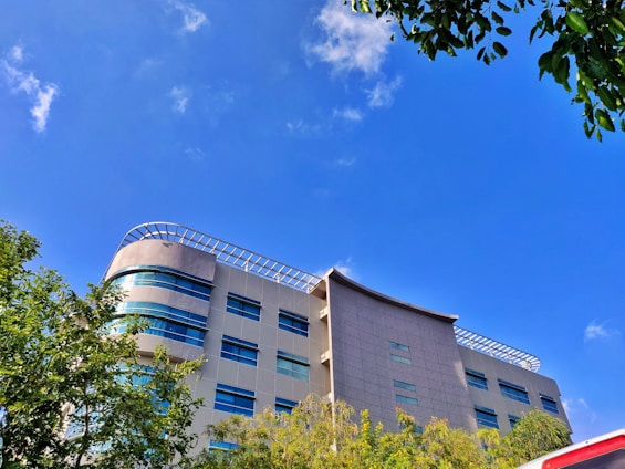 A modern building with clean lines surrounded by lush greenery under a bright sky.