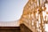 A decorative wrought iron railing with intricate designs and golden accents, extending along a stairway. The image is taken from a low angle, giving prominence to the artistic metalwork against a clear blue sky.