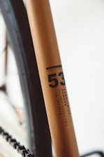 Close-up of a bicycle frame, highlighting details like the model number '53' and descriptors such as 'FabricBike Europe' and 'Hi-Ten Steel 700 Tig Welded'. The frame has a smooth, metallic finish with a minimalist design.