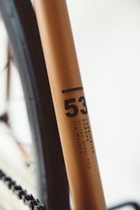 Close-up of a bicycle frame, highlighting details like the model number '53' and descriptors such as 'FabricBike Europe' and 'Hi-Ten Steel 700 Tig Welded'. The frame has a smooth, metallic finish with a minimalist design.