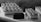 A selection of elegantly arranged desserts, including rectangular pastries with zigzag icing patterns and small chocolate-covered cubes, displayed on a light-colored surface. The image captures a monochromatic aesthetic with a focus on texture and detail.