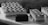 A selection of elegantly arranged desserts, including rectangular pastries with zigzag icing patterns and small chocolate-covered cubes, displayed on a light-colored surface. The image captures a monochromatic aesthetic with a focus on texture and detail.