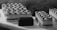 A selection of elegantly arranged desserts, including rectangular pastries with zigzag icing patterns and small chocolate-covered cubes, displayed on a light-colored surface. The image captures a monochromatic aesthetic with a focus on texture and detail.