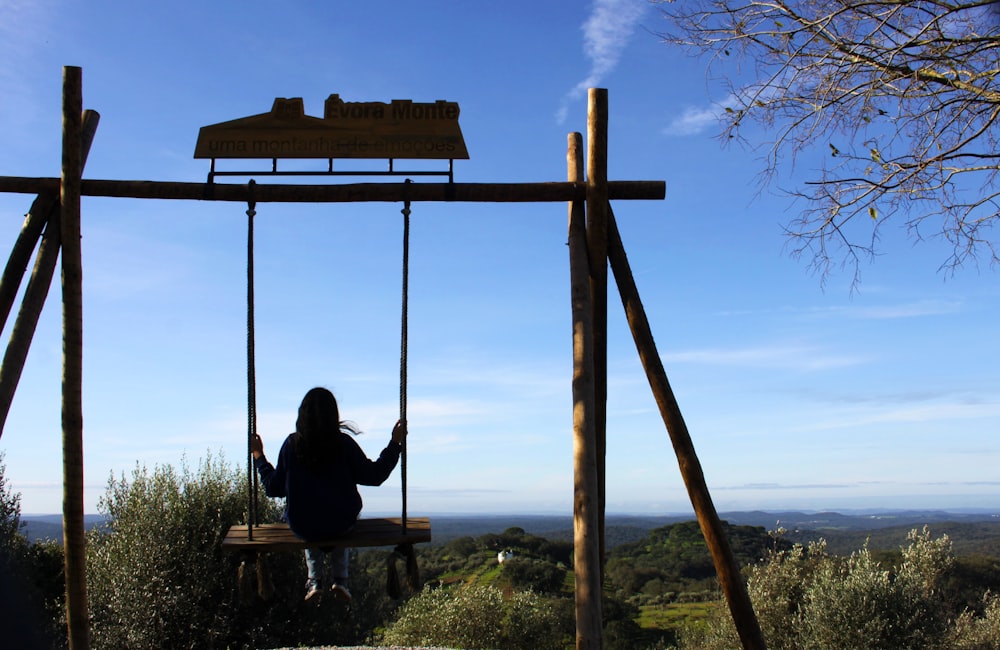 a woman sitting on a wooden swing in the middle of a field