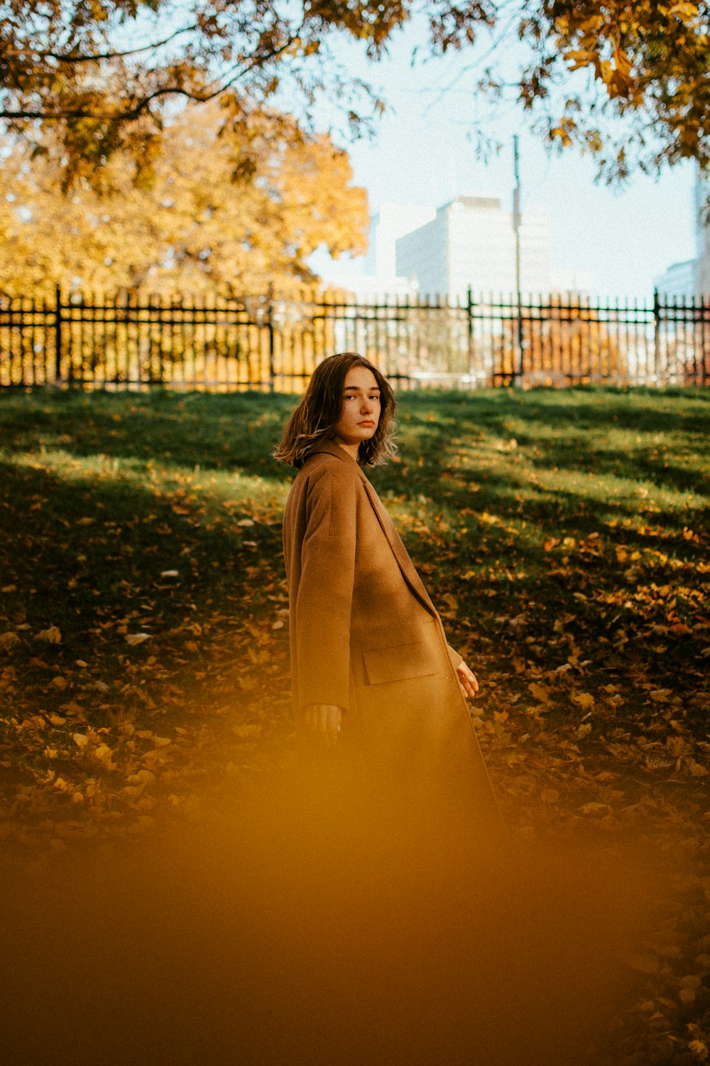 a woman in a brown coat is standing under a tree