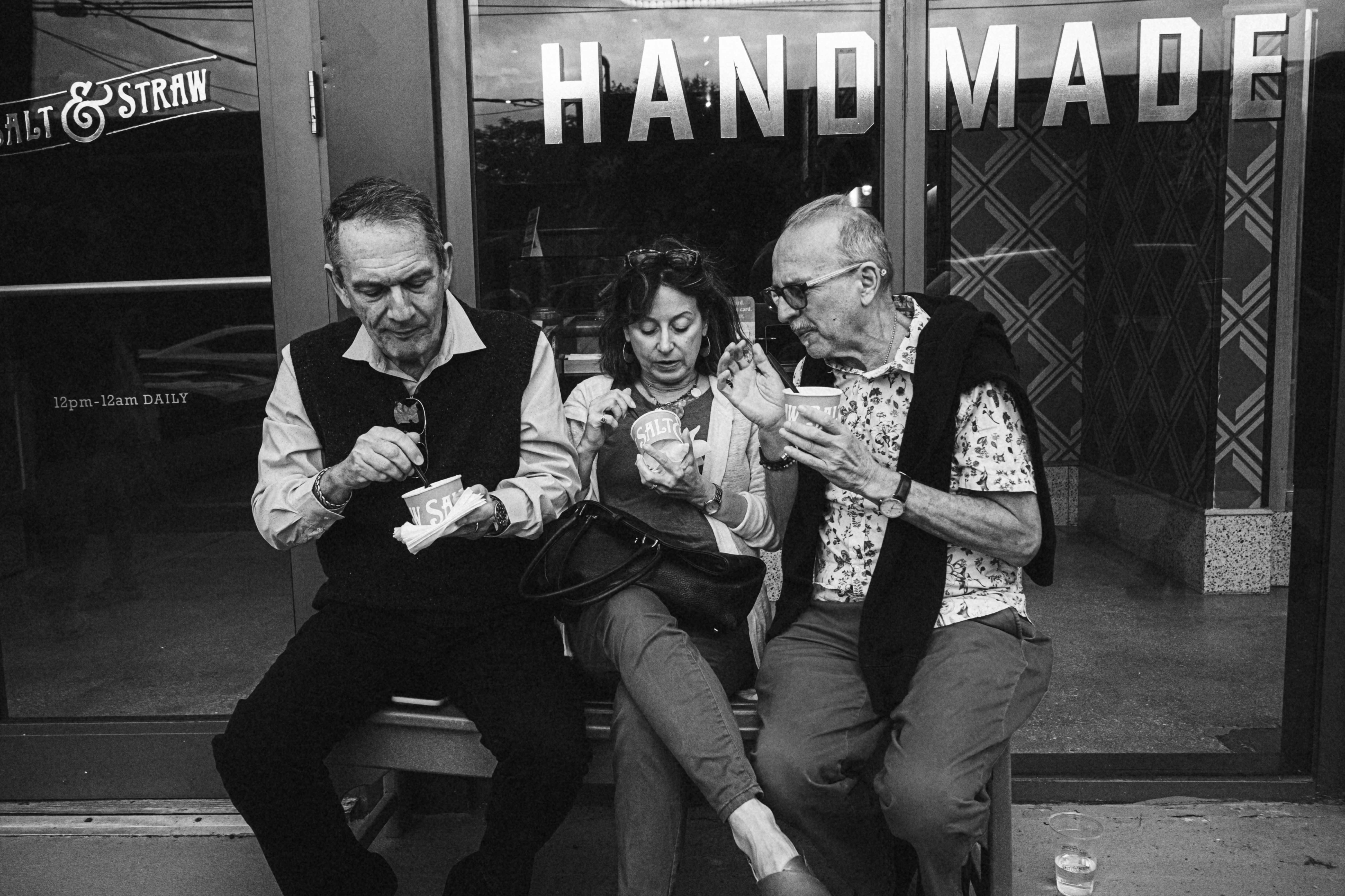 a black and white photo of three people sitting on a bench