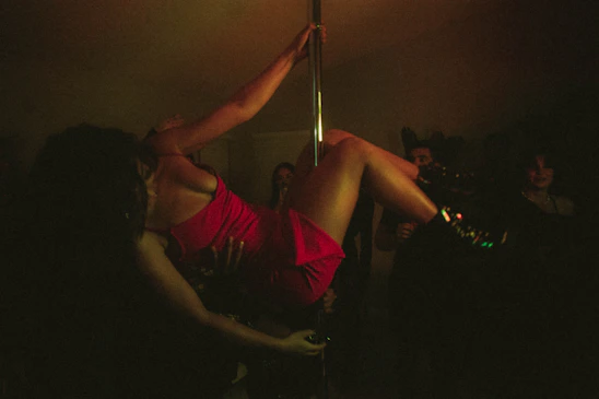 An elegant silhouette of a pole dancer mid-performance, bathed in deep red and gold lighting.