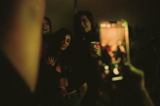 A candid moment of friends taking selfies with bright neon lights in the background.