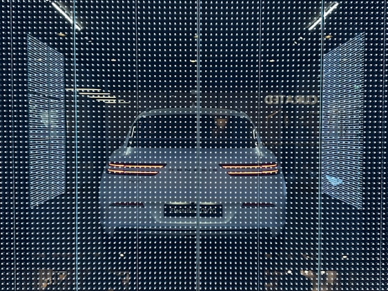 A sleek, dark room illuminated by vibrant neon holograms swirling around a luxury car, showcasing immersive brand activation.