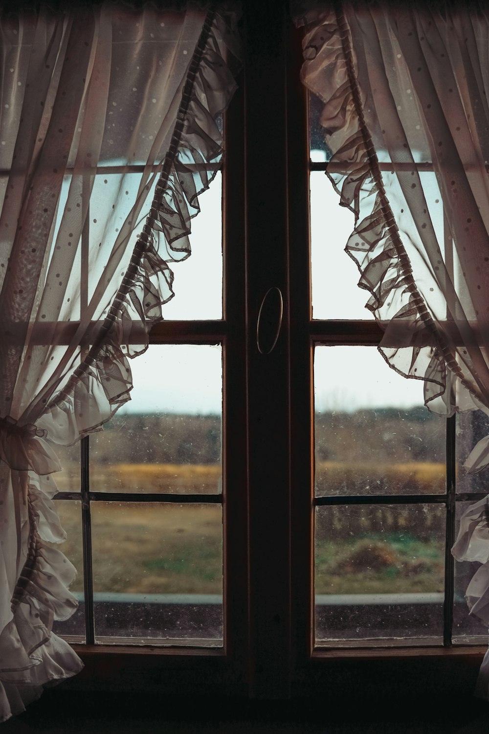 a window with curtains and a view of a field