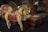 A wooden toy horse with painted details rests on a dark surface. Its body is painted in muted colors with intricate designs on the saddle. In the background, there are various vintage items, including a decorative box with red and green accents, and a carved wooden container.
