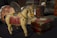 A wooden toy horse with painted details rests on a dark surface. Its body is painted in muted colors with intricate designs on the saddle. In the background, there are various vintage items, including a decorative box with red and green accents, and a carved wooden container.