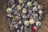 A collection of colorful ceramic drawer knobs with floral and geometric patterns, placed inside a woven basket. The knobs have metal screws attached, and they feature designs in a variety of colors including red, blue, yellow, and green.