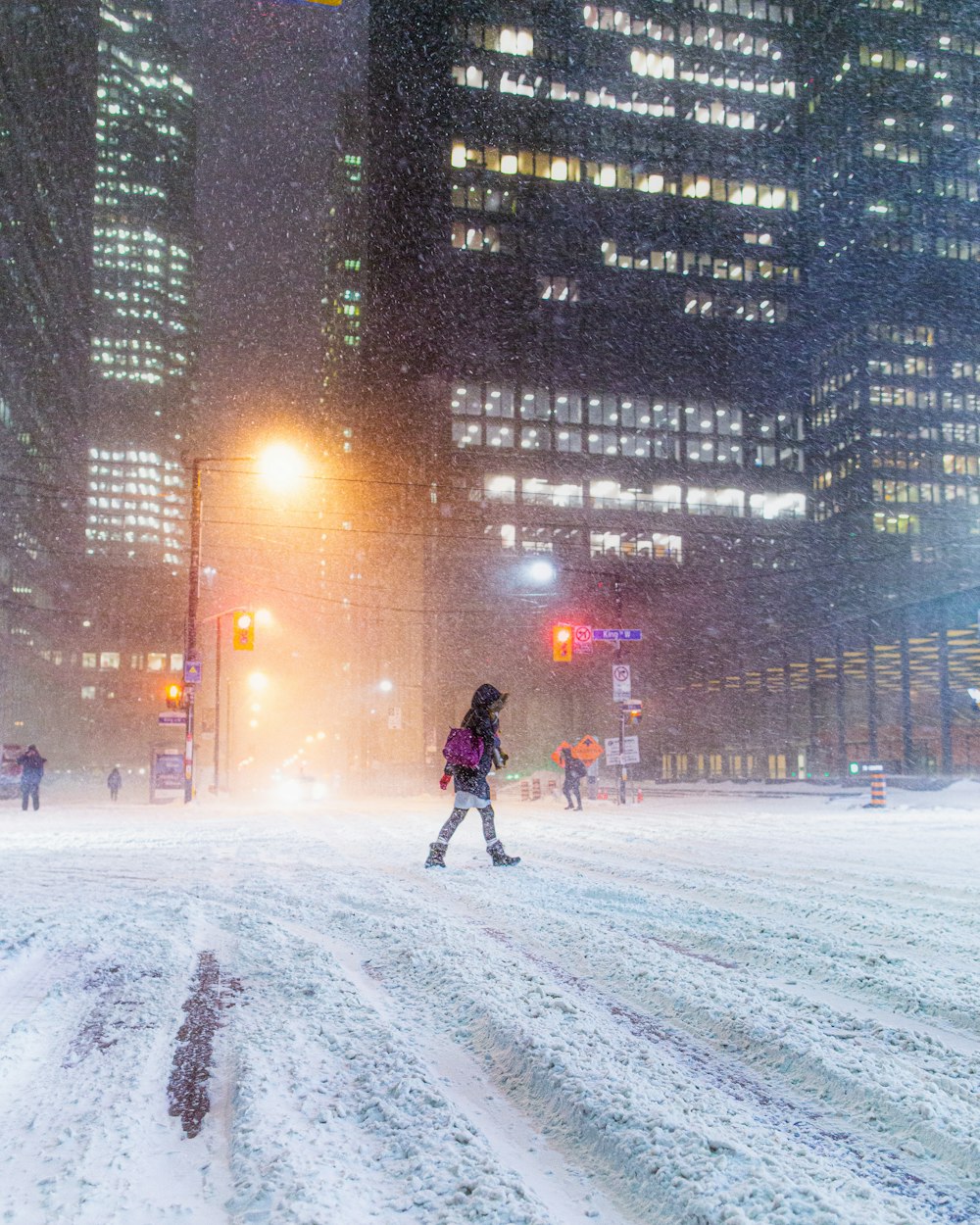 夜に雪に覆われた通りを横切って歩く女性