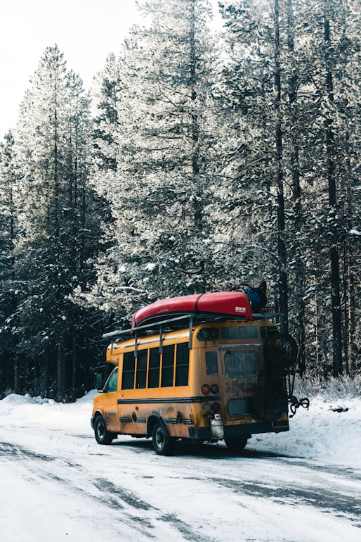 a yellow school bus driving down a snow covered road