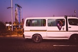 A white Tempo Traveller with large windows cruising on an open road.
