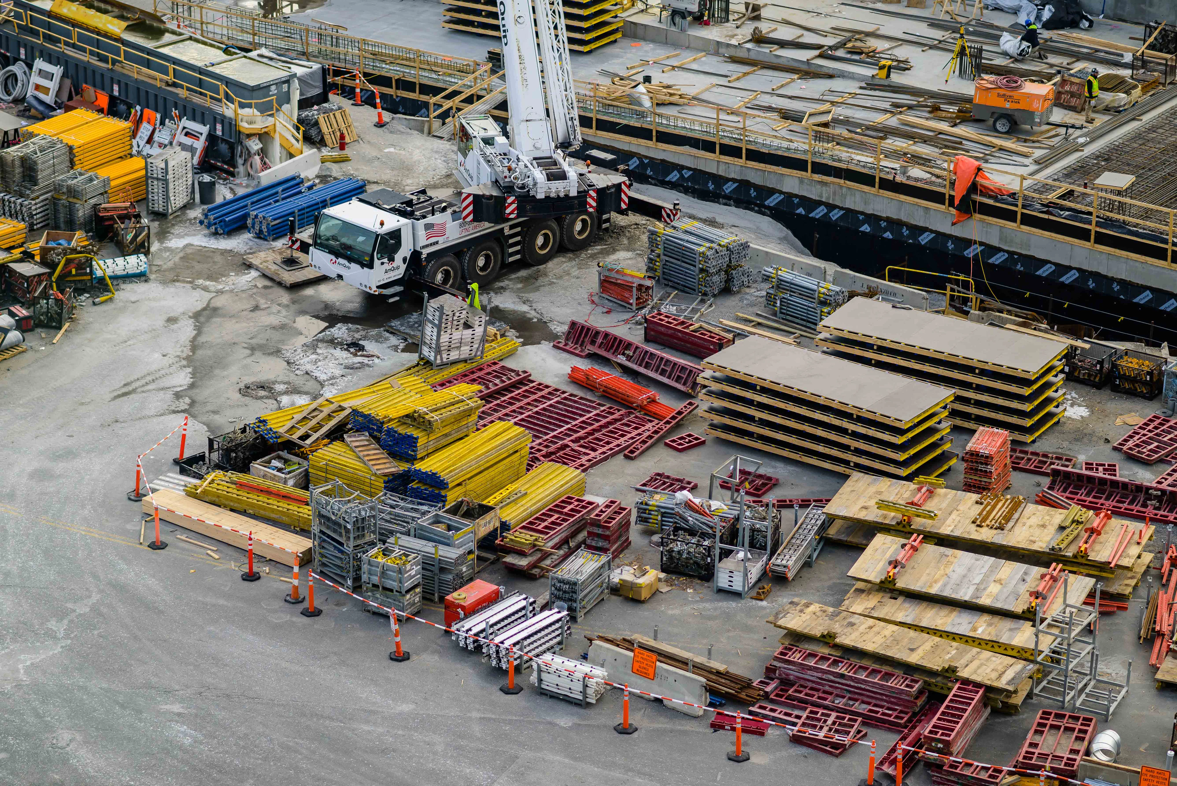 Vista aérea de una obra con materiales acopiados: perfiles, encofrados y una grúa móvil