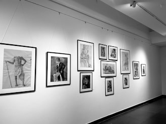 A gallery wall features a series of framed black and white sketches and drawings. The collection includes various portraits and studies of human figures in different poses, with some sketches showing detailed expressions and postures.