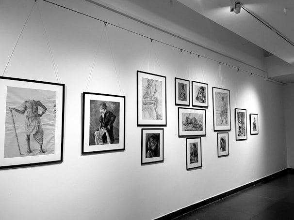 A gallery wall features a series of framed black and white sketches and drawings. The collection includes various portraits and studies of human figures in different poses, with some sketches showing detailed expressions and postures.