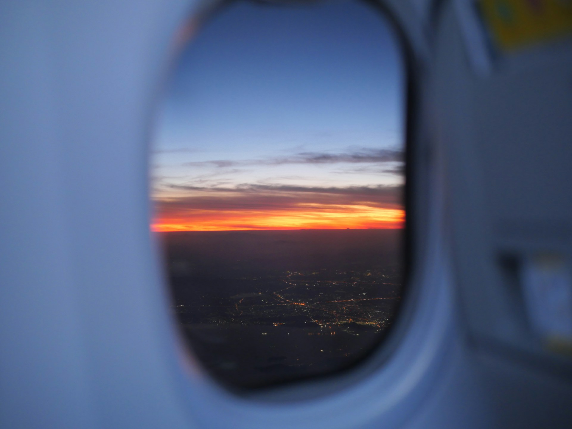 A vibrant sunset view from an airplane window showing a city skyline below.