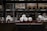 A warehouse shelf filled with packaged rolls of material. The rolls are arranged neatly on metal racks, surrounded by boxes and pallets. The lighting is dim, creating a sense of depth and storage abundance.