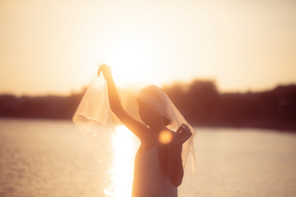 a woman with a veil on her head standing in front of a body of water