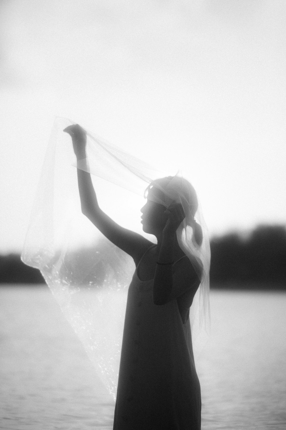 a woman standing in the water holding a veil over her head