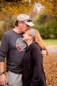 A candid moment of the couple exchanging smiles beneath a canopy of autumn leaves.