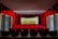 A small, intimate theater with red velvet seats arranged in rows facing a stage with a closed curtain. The walls are covered in matching red velvet paneling, and there are decorative lamps on the side walls. The stage is framed with a red curtain and light-colored backdrop.
