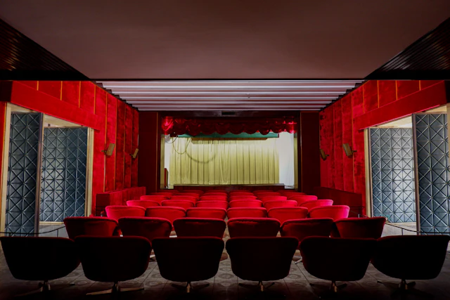 Large auditorium with red velvet seats arranged in rows facing a professional stage with curtains