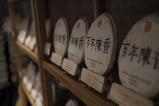 Several circular packages are displayed on a wooden shelf, each wrapped in paper with Chinese characters printed on them. The packages appear to be for tea or a similar product, and they are organized neatly with labels beneath.