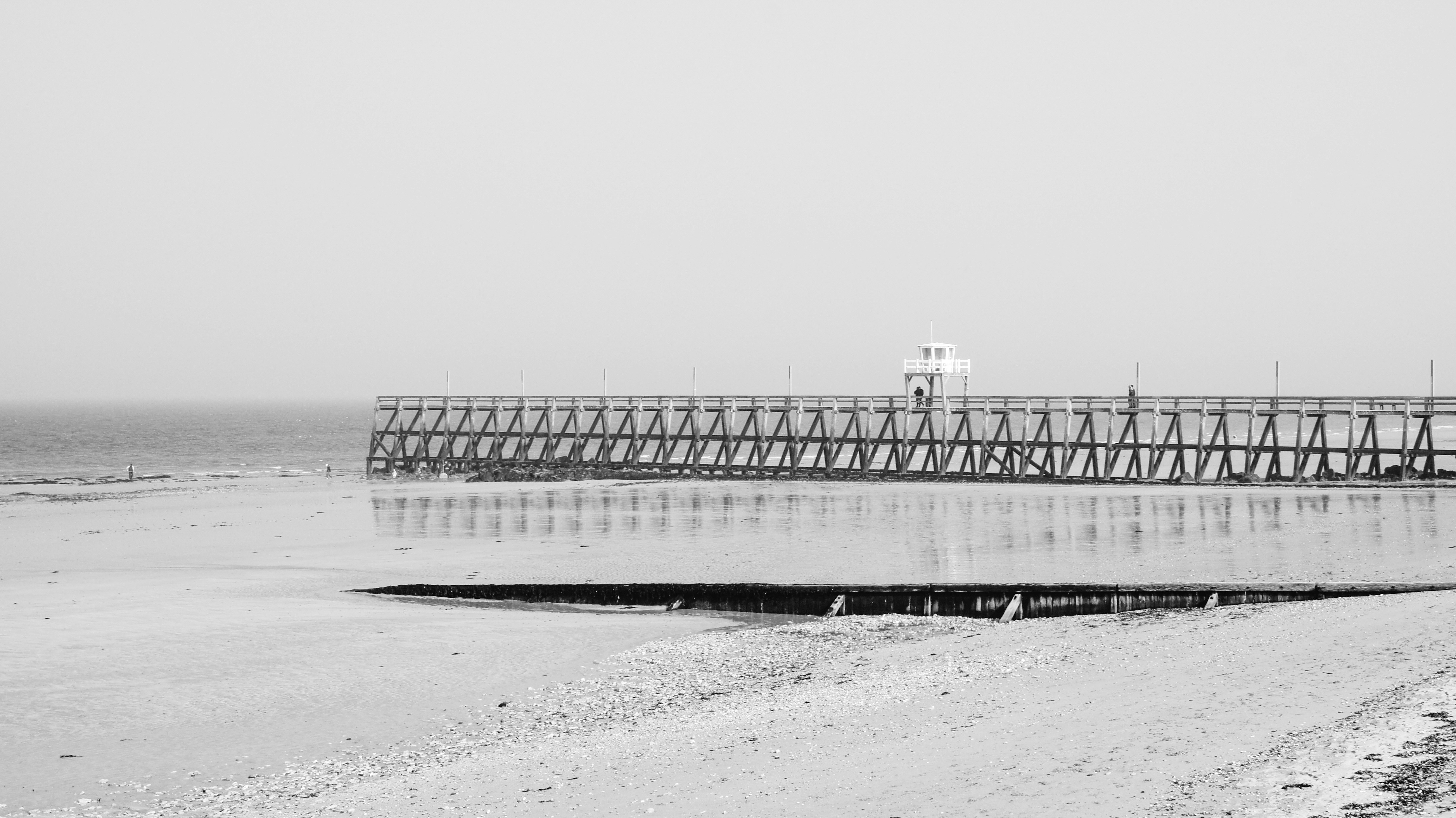 a black and white photo of a pier on the beach