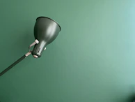 Close-up of a sculptural floor lamp with matte forest green accents against a crisp parchment wall.
