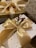 A close-up view of elegantly wrapped gifts featuring large gold satin bows and festive decorations such as a small sprig of red and white berries. The boxes have a luxurious appearance with one adorned in gold and the other with a white and gold polka dot pattern. Another box with a patterned design is partially visible.