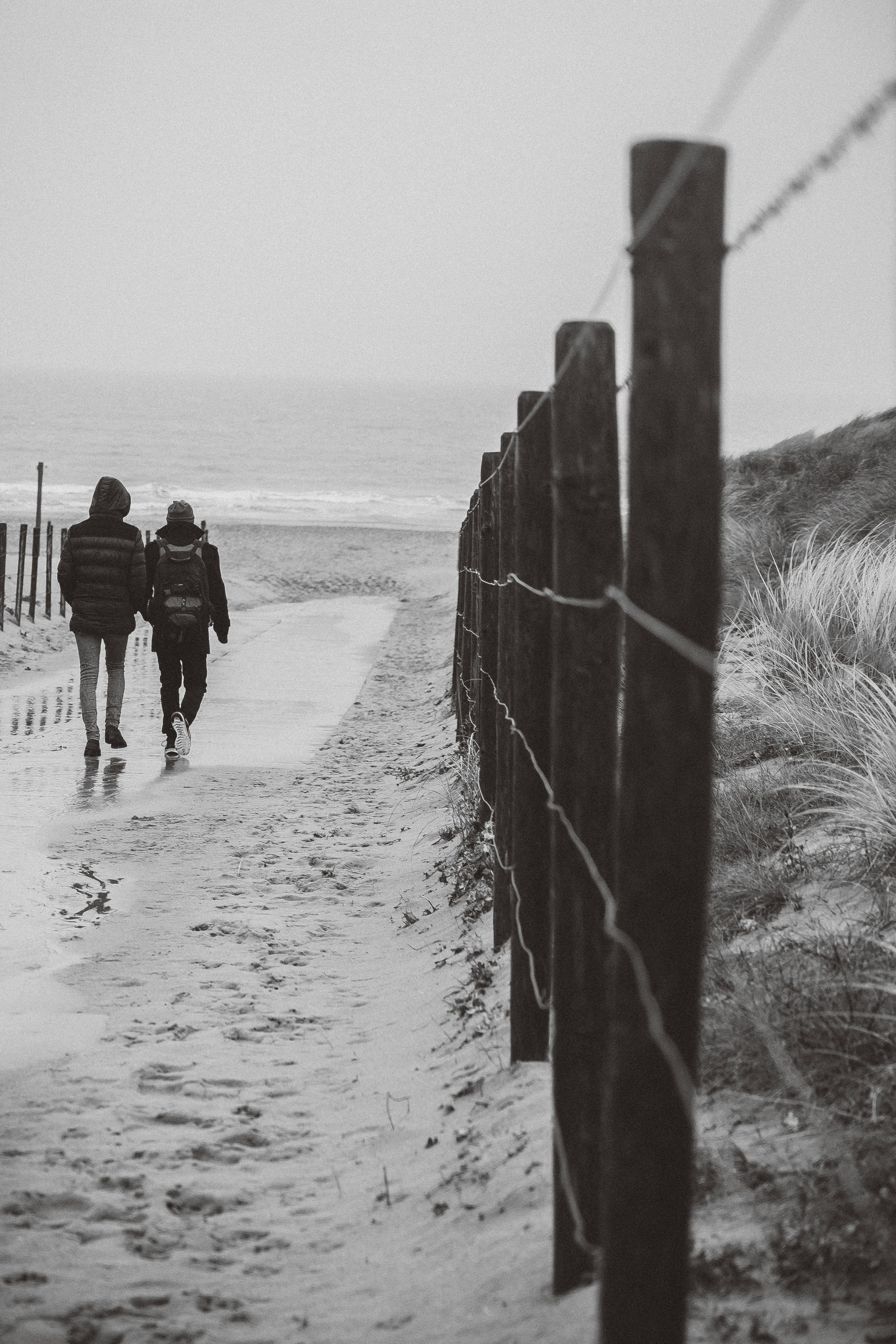 a couple of people walking down a beach next to a fence