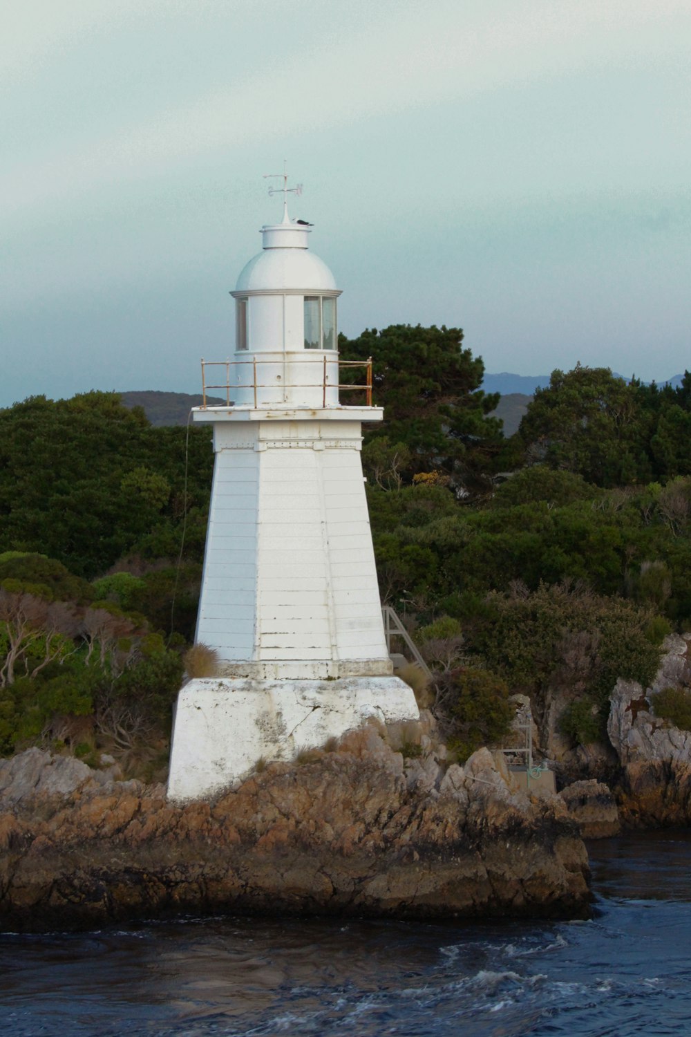 a white lighthouse sitting on top of a rock next to a body of water