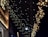 Strings of twinkling warm white fairy lights are hanging in cascading patterns against a dark background, creating a festive and enchanting atmosphere. The soft glow of the lights illuminates part of the building facade they are attached to.