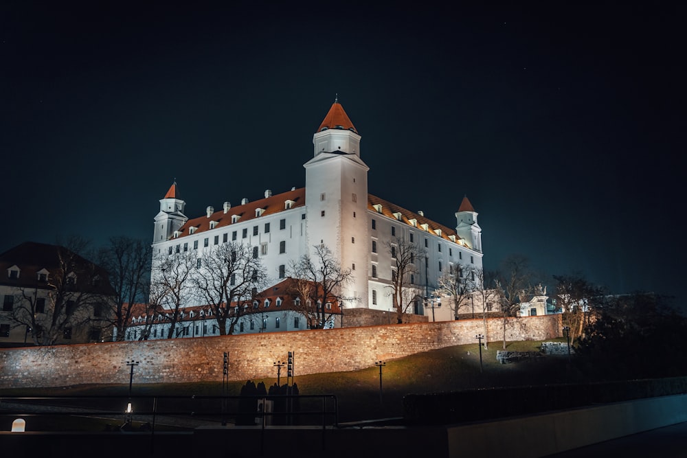 Un castillo iluminado por la noche con gente caminando por los alrededores