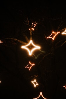 A dark background with illuminated, star-shaped lights glowing in a warm, golden hue. The lights are scattered in a pattern that evokes a sense of whimsy or festive decoration.
