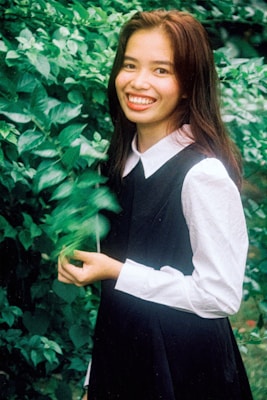 A model wearing a simple, stylish outfit, standing in a lush garden with a warm smile.