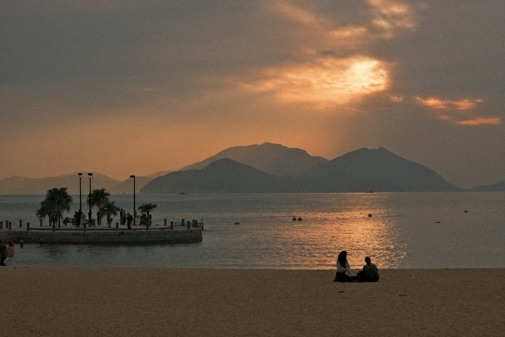 a couple of people sitting on top of a sandy beach