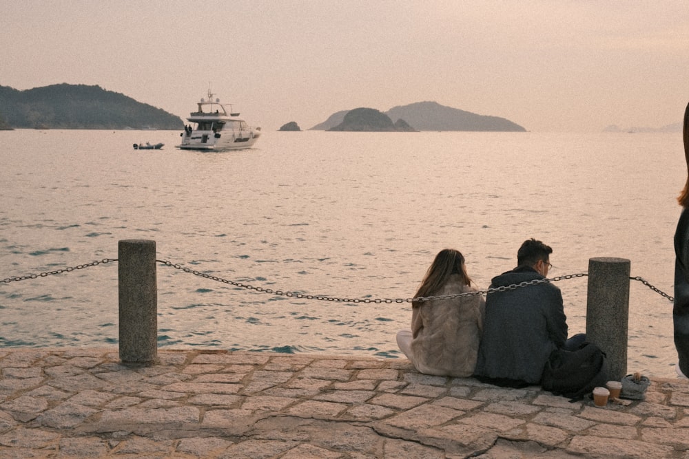 a man and a woman sitting on a dock next to a body of water