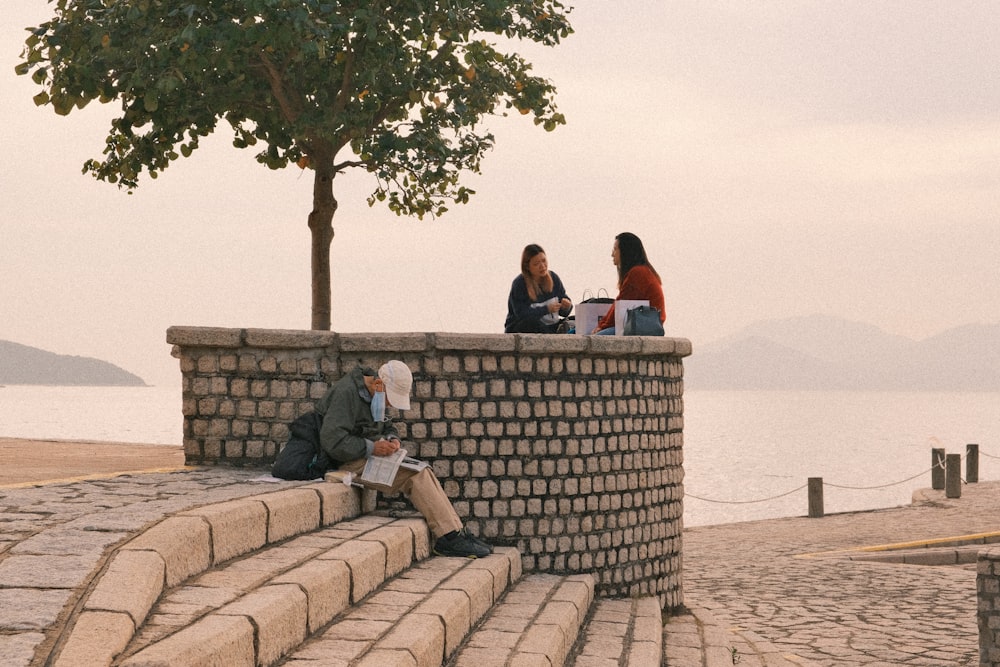 a group of people sitting on top of a stone wall