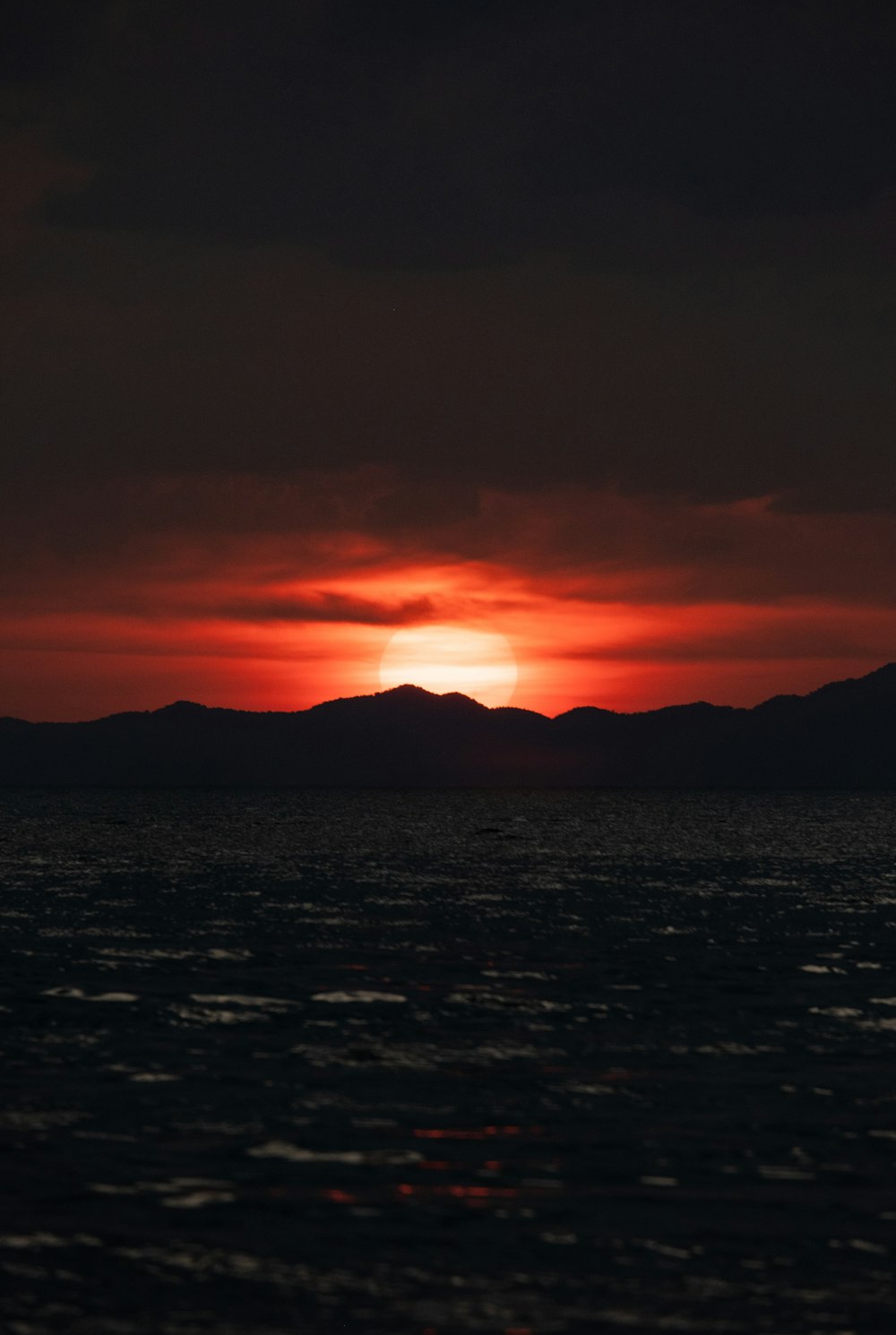 the sun is setting over the ocean with mountains in the distance